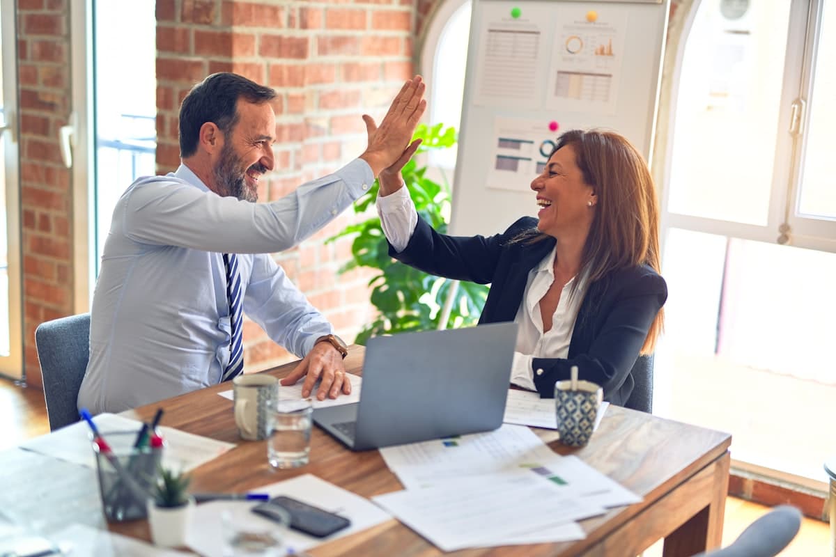 Two business professionals high-fiving over laptop in office
